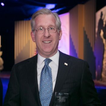 A man in a suit and tie smiles at an event, possibly related to the Navy SEAL Foundation New York City Benefit Dinner.