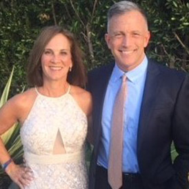 A man and a woman are smiling outdoors, dressed in formal attire.