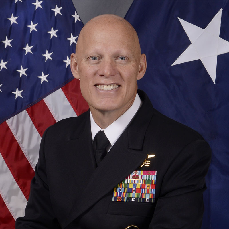 Vice Admiral Sean Pybus in a military uniform stands in front of U.S. flags.