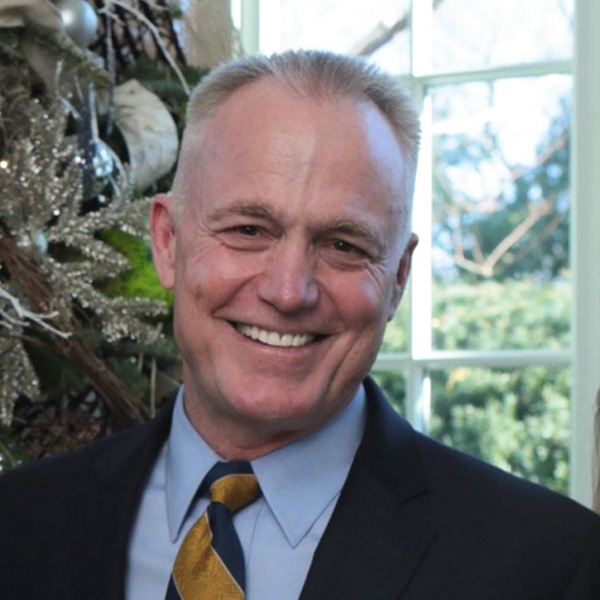 Vice Admiral P. Gardner Howe, III, USN (Ret.) smiling in a suit with a festive background.