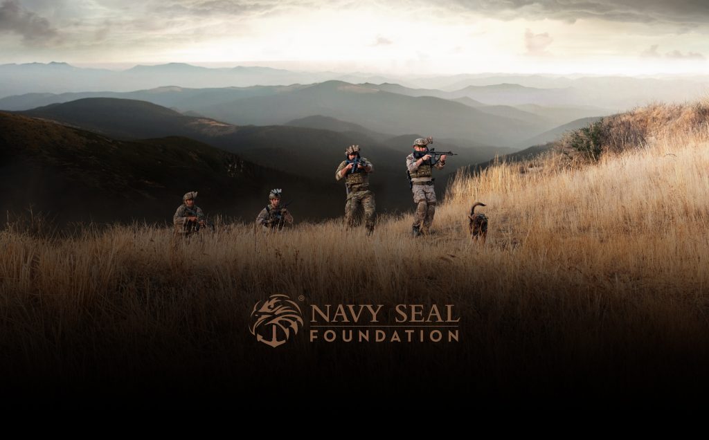 Navy SEALs are moving through a grassy field with mountains in the background, featuring the "Navy Seal Foundation" logo.