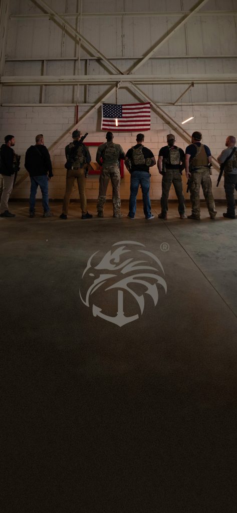 A group of people stand facing a wall with the American flag, and a logo is on the floor.